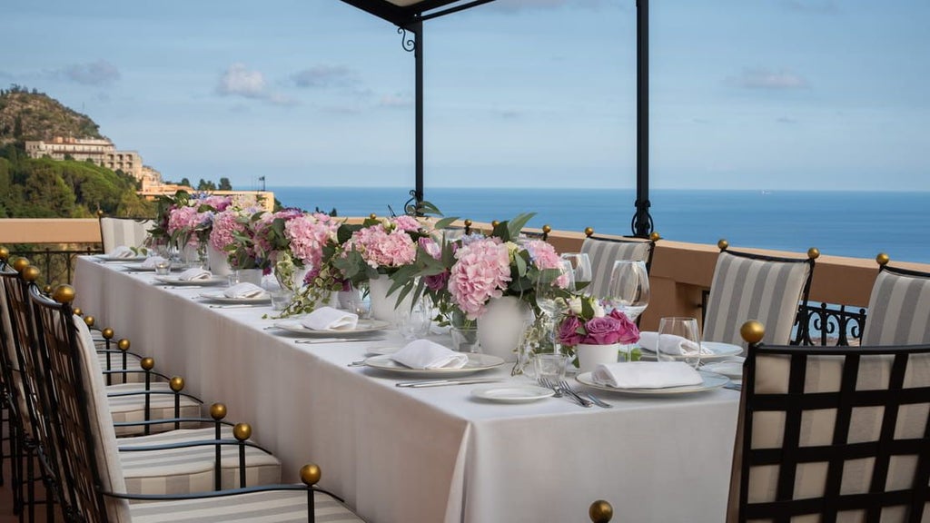 Grand cliffside hotel in Taormina with stone archways and manicured gardens overlooking the Ionian Sea and Mount Etna in Sicily