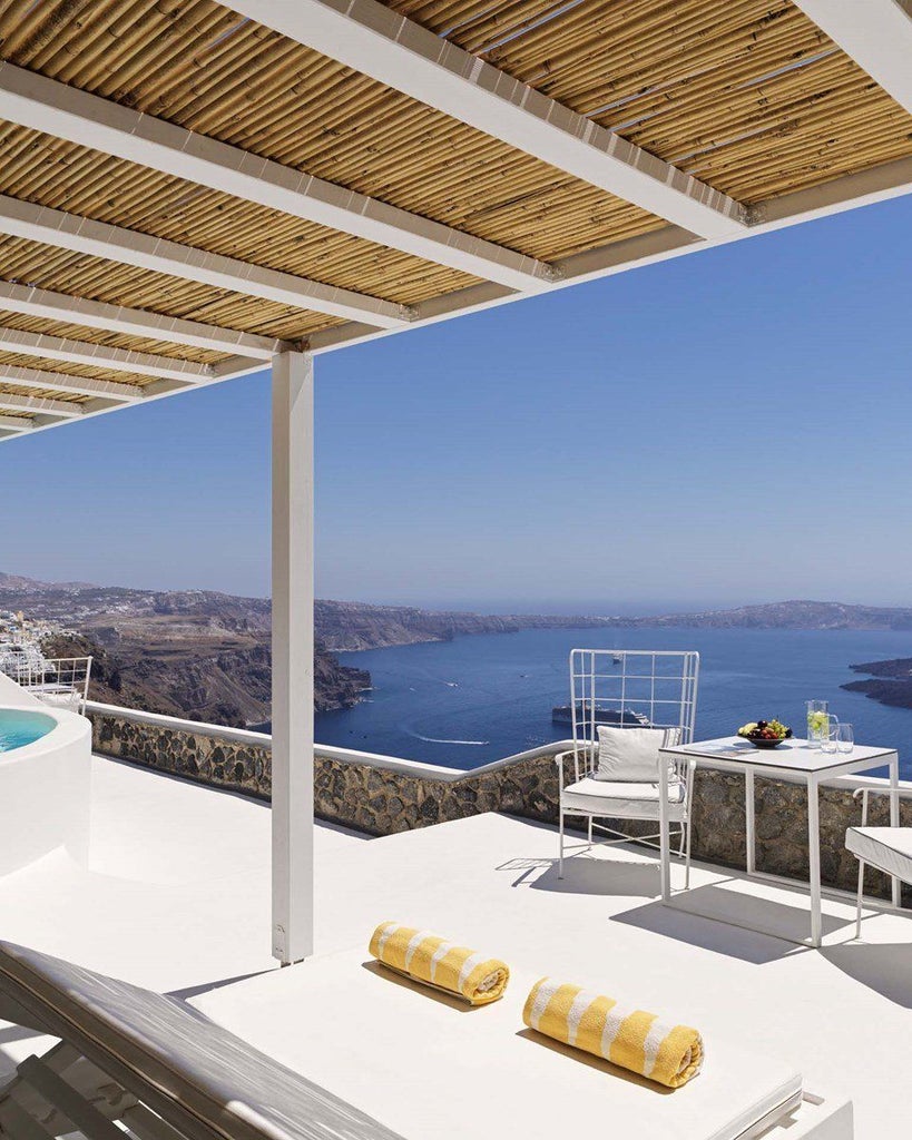 Luxury white-walled Santorini suite with private outdoor jetted tub overlooking azure Aegean Sea, featuring minimalist Cycladic architectural design