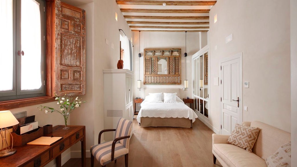 Elegant Spanish boutique hotel with arched wooden doors, wrought iron balconies and cream facade set on narrow cobblestone street