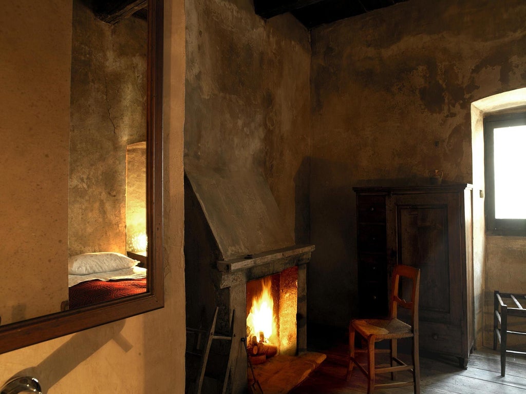 Rustic Italian stone room with vaulted ceiling, antique wooden bed, and panoramic window overlooking historic bell tower in Santo Stefano di Sessanio