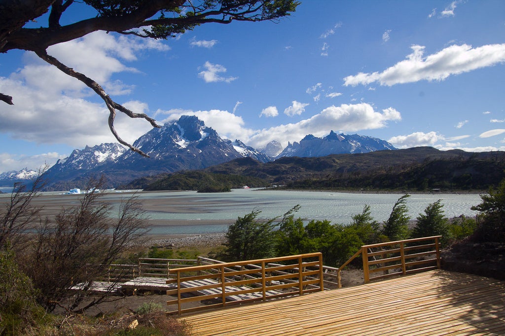 Modern four-star hotel building with glass windows nestled between mountains and forests, overlooking glacial Grey Lake in Torres del Paine