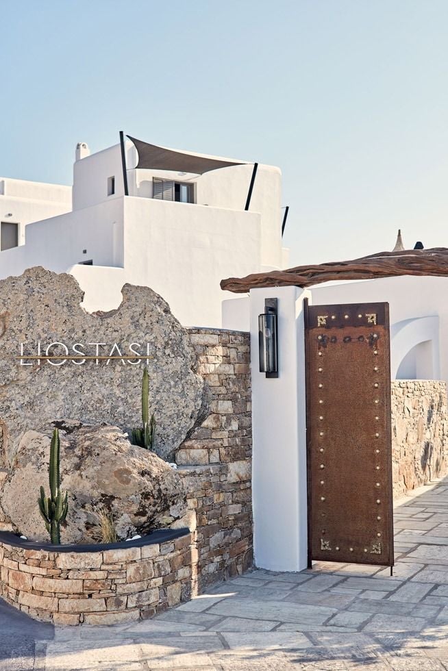 Infinity pool overlooking Aegean Sea at sunset, with white Cycladic architecture and elegant lounge chairs on stone terrace