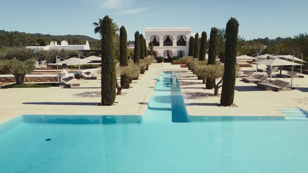 Luxurious white-walled boutique hotel with minimalist design, featuring a tranquil pool surrounded by Mediterranean landscape in Ibiza, Spain