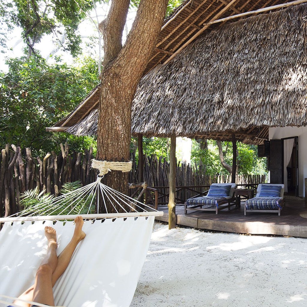 Luxurious coastal Kenyan cottage with thatched roof, white linens, tropical wooden furniture, and ocean view from private veranda at scenset resort