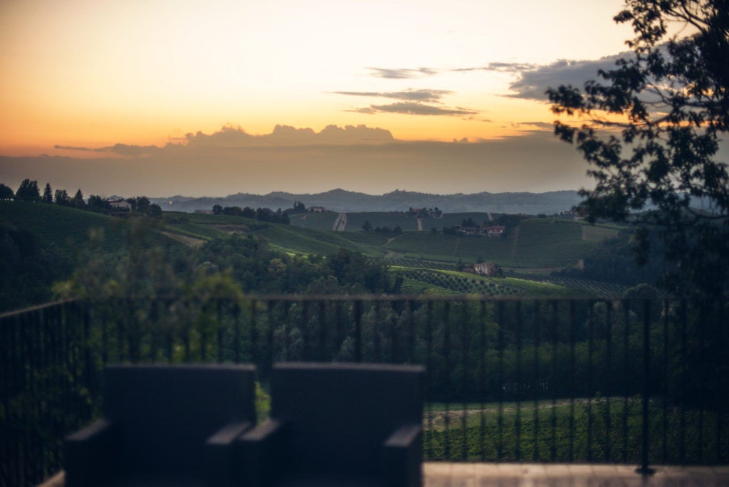 Luxurious Italian countryside hotel with terracotta-tiled roofs, stone facade, and lush cypress trees against a golden sunset backdrop