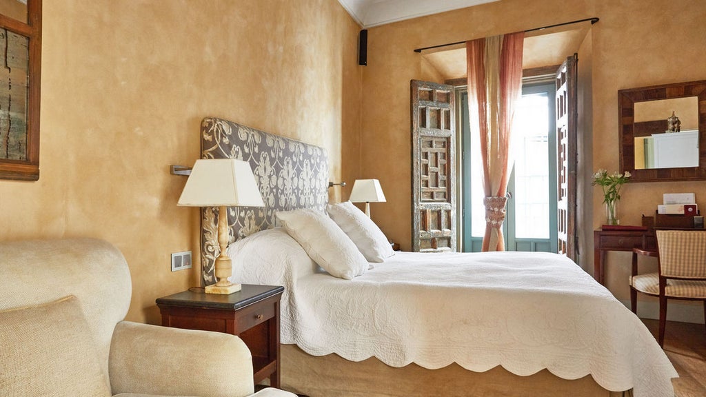 Elegant Spanish boutique hotel with white-washed walls, wrought-iron balconies and potted plants along a narrow cobblestone street