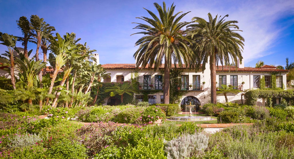 Spanish colonial-style waterfront resort with white stucco walls, red-tiled roofs, palm trees and manicured gardens overlooking Pacific Ocean