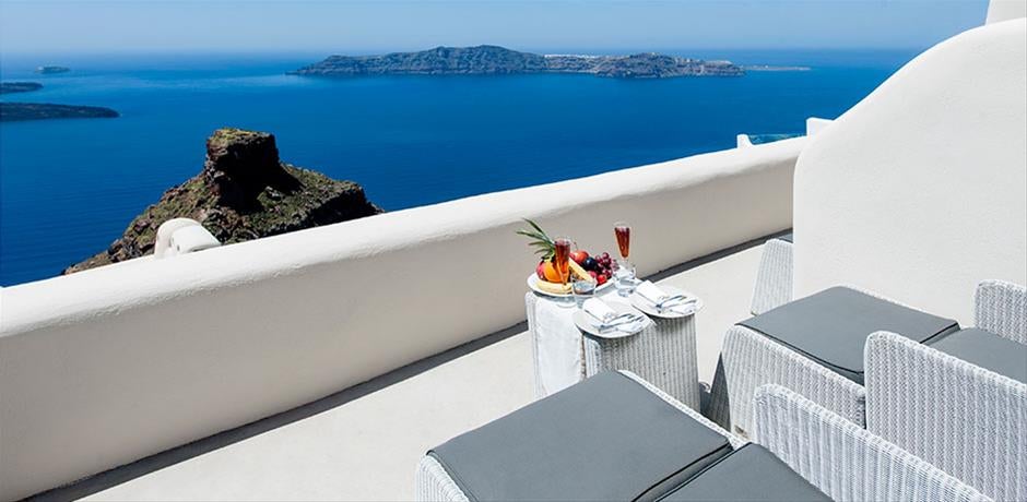 Whitewashed luxury cave hotel in Santorini with infinity pool overlooking Aegean Sea, carved into volcanic cliffs at sunset