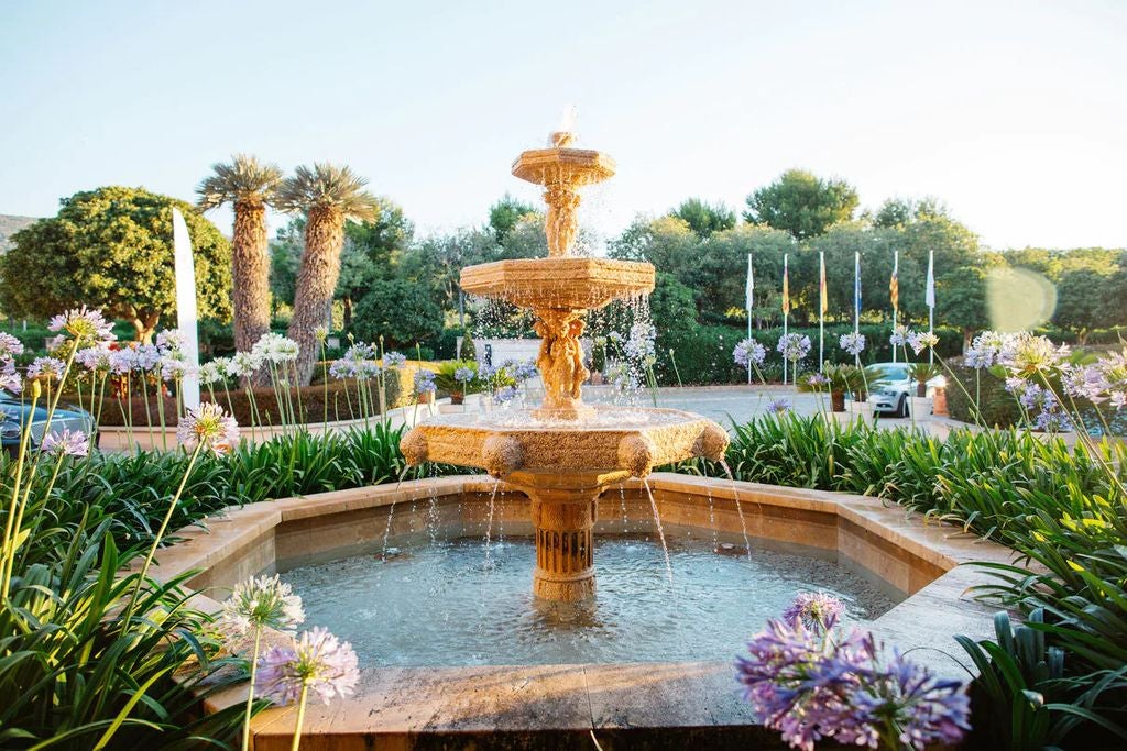 Elegant Mediterranean resort with white stone facade, palm trees, and luxurious pool terrace overlooking Mallorca's turquoise coastline