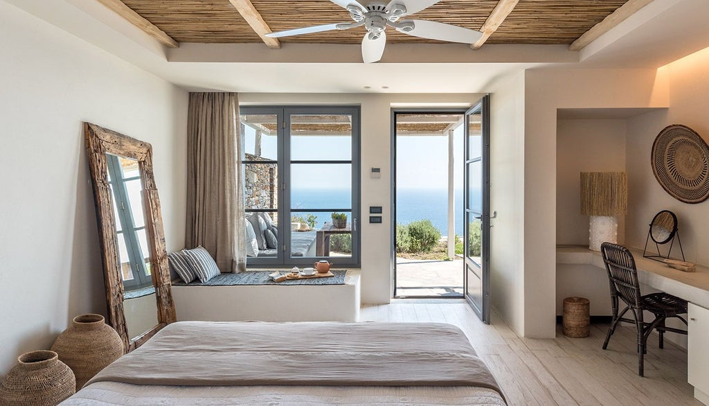 Sleek white minimalist bedroom with panoramic Aegean Sea view, featuring clean lines, modern furniture, and a private balcony overlooking scenic Greek landscape.