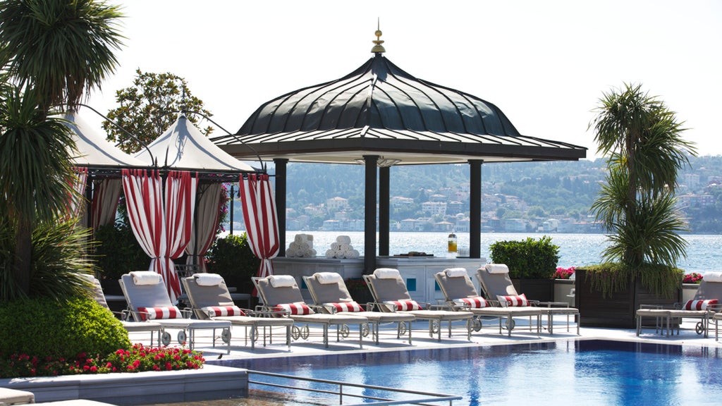 Elegant white Ottoman palace hotel overlooking Bosphorus strait with illuminated terrace, manicured gardens and waterfront pool