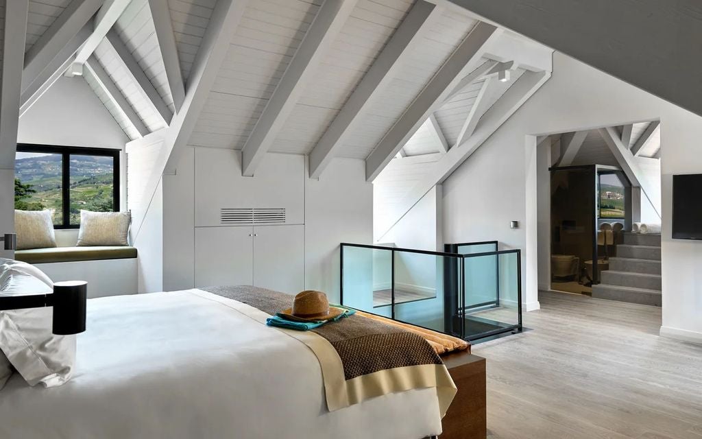 Modern duplex suite with wood-beamed ceiling, white walls, plush king bed, floor-to-ceiling windows overlooking Douro Valley vineyards