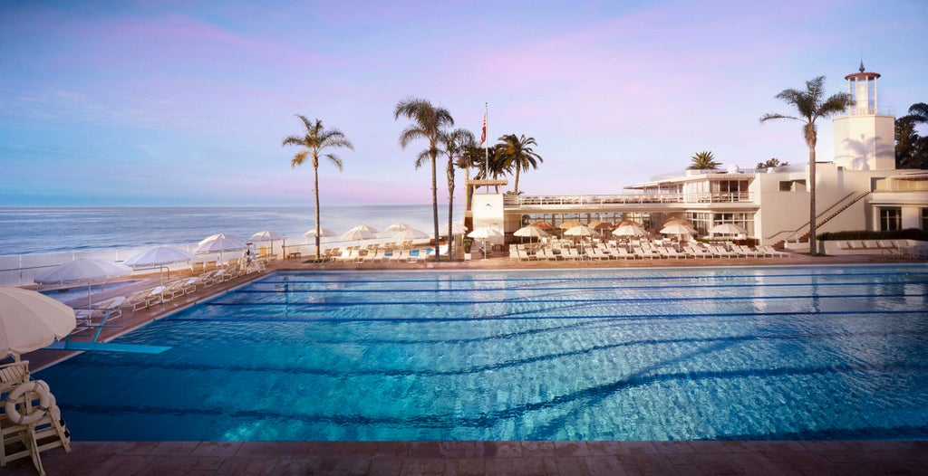 Spanish Colonial-style beachfront hotel with white stucco walls, red-tiled roofs, and lush tropical gardens overlooking Pacific coast at sunset