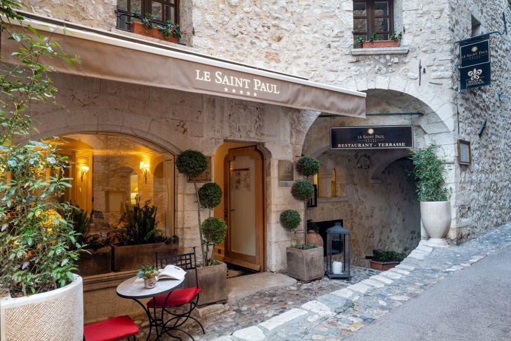 Elegant boutique hotel facade in Saint-Paul-de-Vence, stone walls, terracotta roof, lush greenery, charming French Riviera architectural style