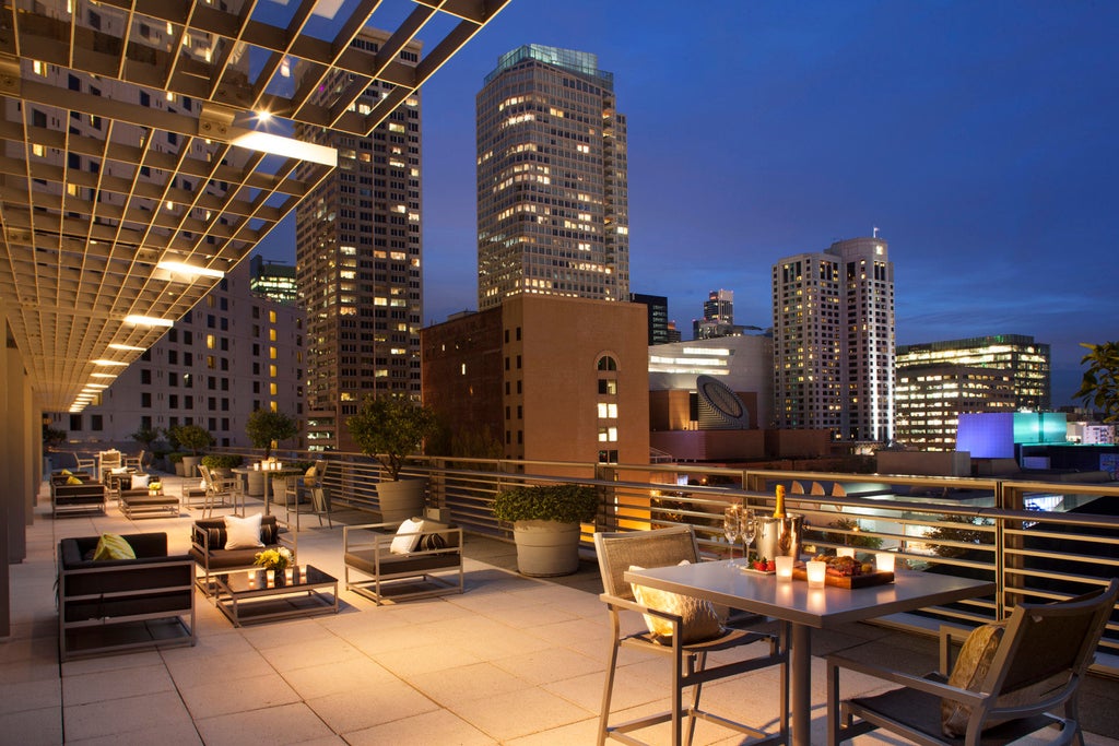 Contemporary high-rise luxury hotel tower with glass facade, illuminated at dusk against San Francisco skyline and Bay Bridge vista