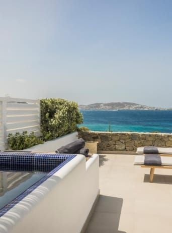 Luxurious white-washed Cycladic hotel with infinity pool overlooking azure Aegean Sea, showcasing elegant minimalist design of Scenset Mykonos resort