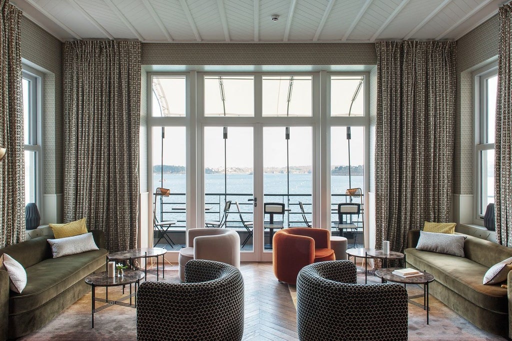 Luxurious coastal hotel with blue-gray facade perched on rocky cliff overlooking azure waters near Dinard, Brittany, France.