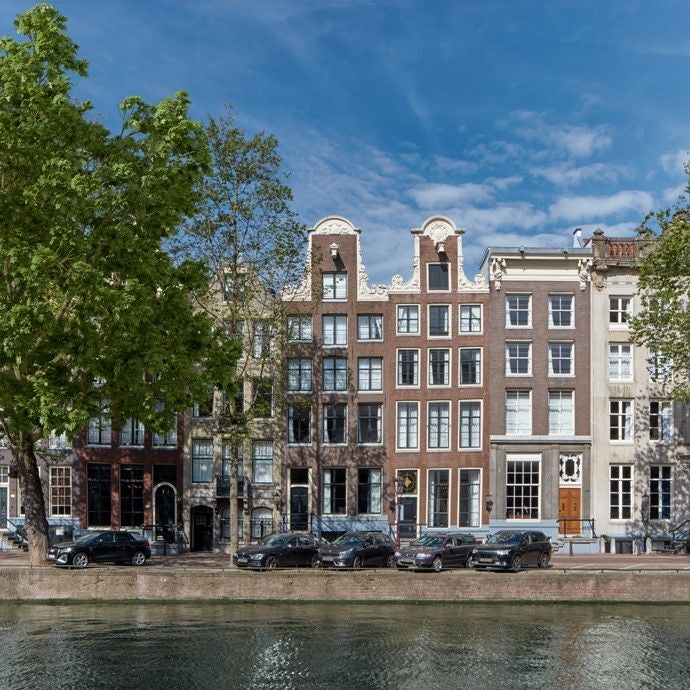 Historic canal house converted into luxury hotel Pulitzer Amsterdam, with elegant brick facade and charming flower boxes along waterfront