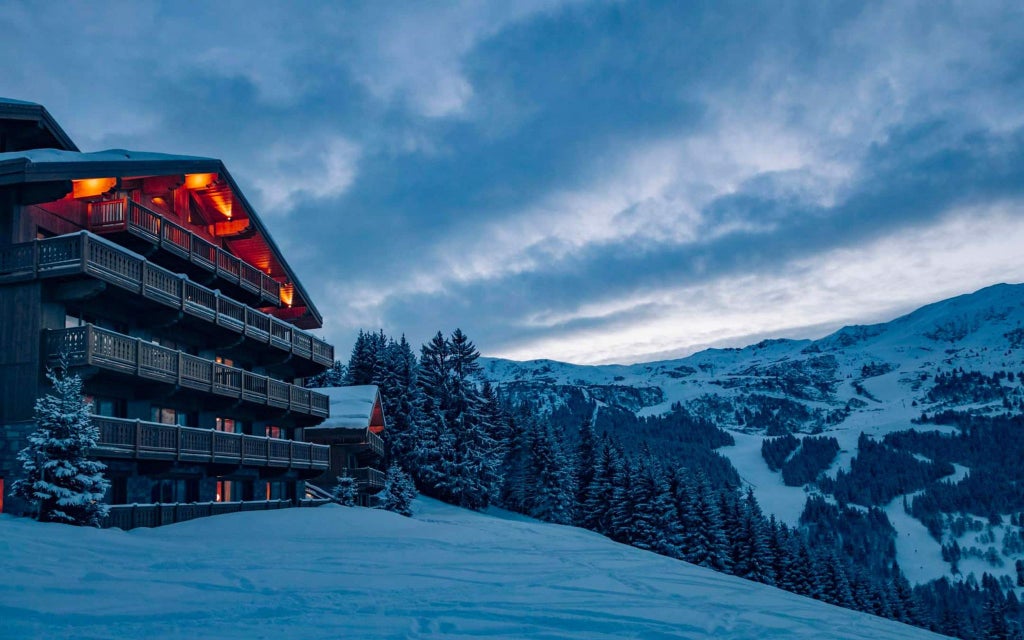 Luxurious Alpine chalet-style hotel nestled in snow-covered Méribel mountains, with modern wood and glass architecture, elegant winter landscape backdrop