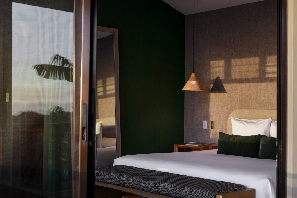 Elegant premium suite at Senda Monteverde Hotel featuring modern minimalist design, natural wood accents, and panoramic forest view through large windows.