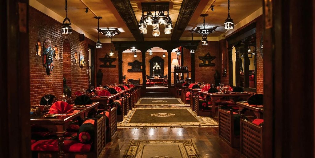 Historic Nepalese luxury hotel with ornate wooden carvings, traditional red brick architecture and courtyard featuring carved pillars