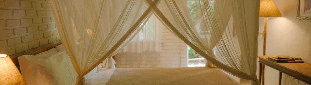 Elegant Brazilian boutique hotel suite with white linens, wooden furniture, tropical decor, and natural light streaming through large windows overlooking lush scenery