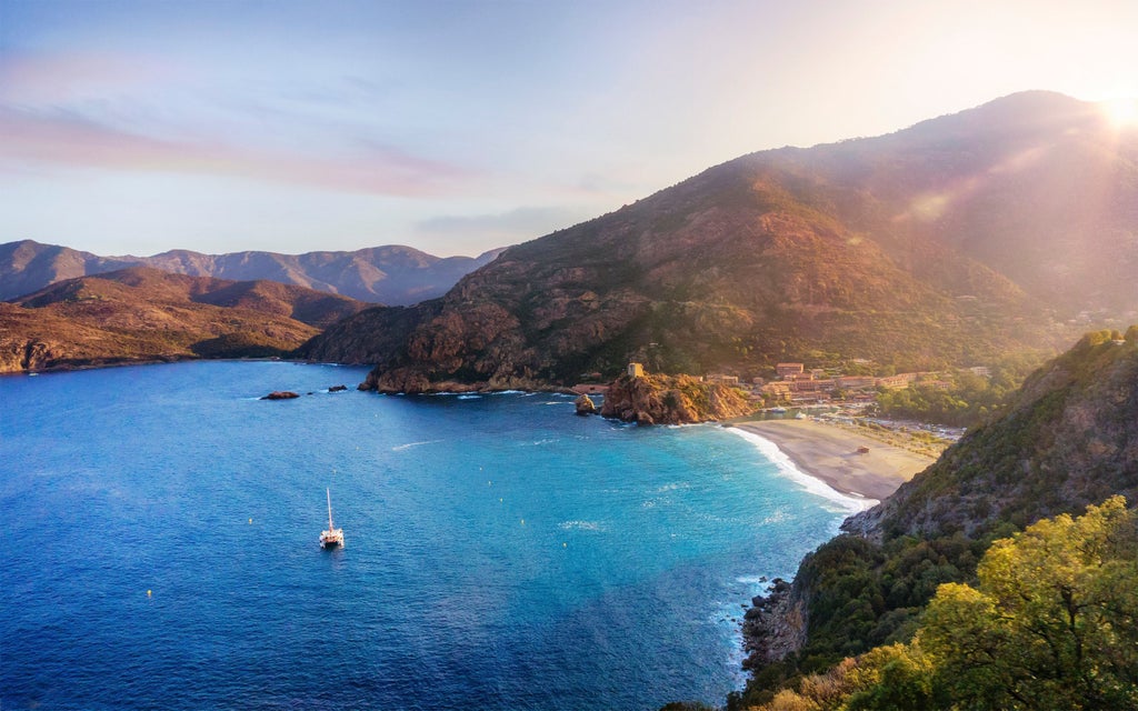 Mediterranean coastal resort town in Corsica with luxury villas cascading down hillside overlooking turquoise bay at sunset