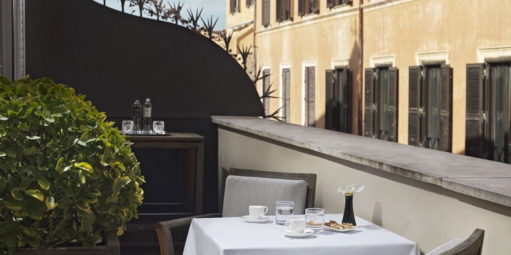 Elegant balcony room at luxurious JK Place Roma, featuring plush white linens, marble details, and a sun-drenched terrace overlooking historic Italian architecture