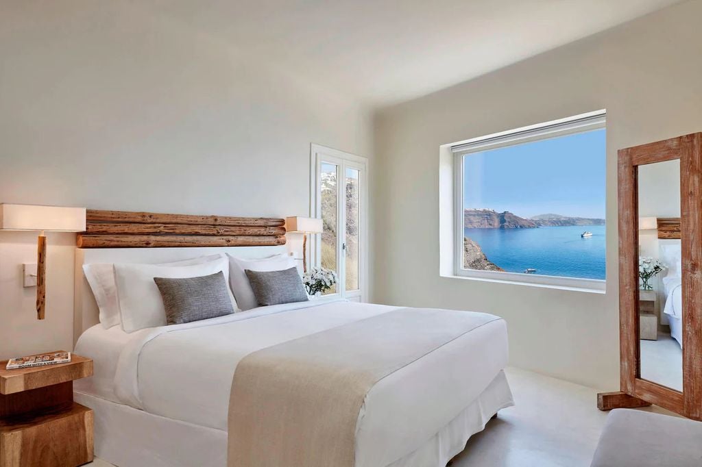 Whitewashed luxury villa with infinity pool overlooking Santorini's caldera, framed by curved architecture and Mediterranean blue sky