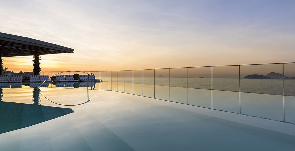 Elegant ocean-view infinity pool atop Hotel Fasano Rio, overlooking Ipanema Beach with mountain silhouettes in sunset background