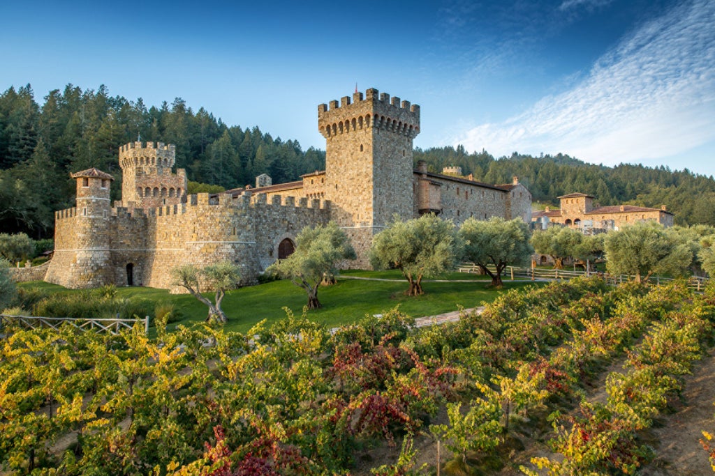 Elegant stone building of Four Seasons Napa Valley nestled among vineyards, with mountain backdrop and luxurious outdoor terrace seating