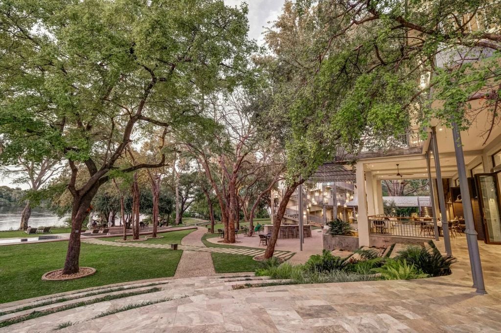 Grand colonial-style hotel with white exterior and palm trees, overlooking serene Zambezi River in Zimbabwe's lush landscape at sunset