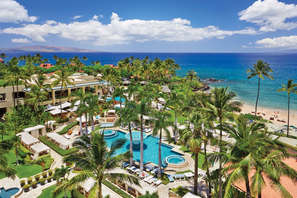 Beachfront luxury resort in Maui with infinity pool overlooking Pacific Ocean, palm trees, and private cabanas under golden sunset sky