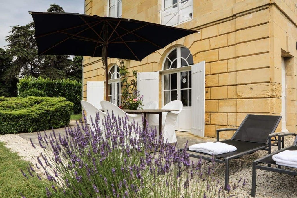 Luxurious French countryside suite with elegant wooden furnishings, soft cream linens, and large windows overlooking verdant landscape at Château les Merles