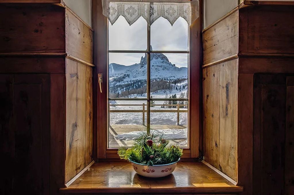 Historic mountain lodge with wooden balconies nestled beneath dramatic Dolomite peaks, surrounded by alpine meadows at sunset