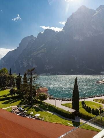 Elegant Art Nouveau hotel facade with Lake Garda backdrop, featuring ornate white balconies and lush green gardens in scenic Italian landscape