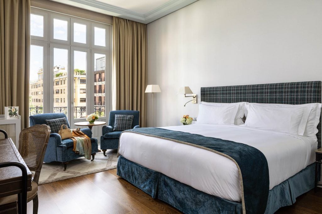 Elegant junior suite with modern minimalist design, featuring plush white bedding, wooden floor, and soft natural lighting in luxury Spanish hotel