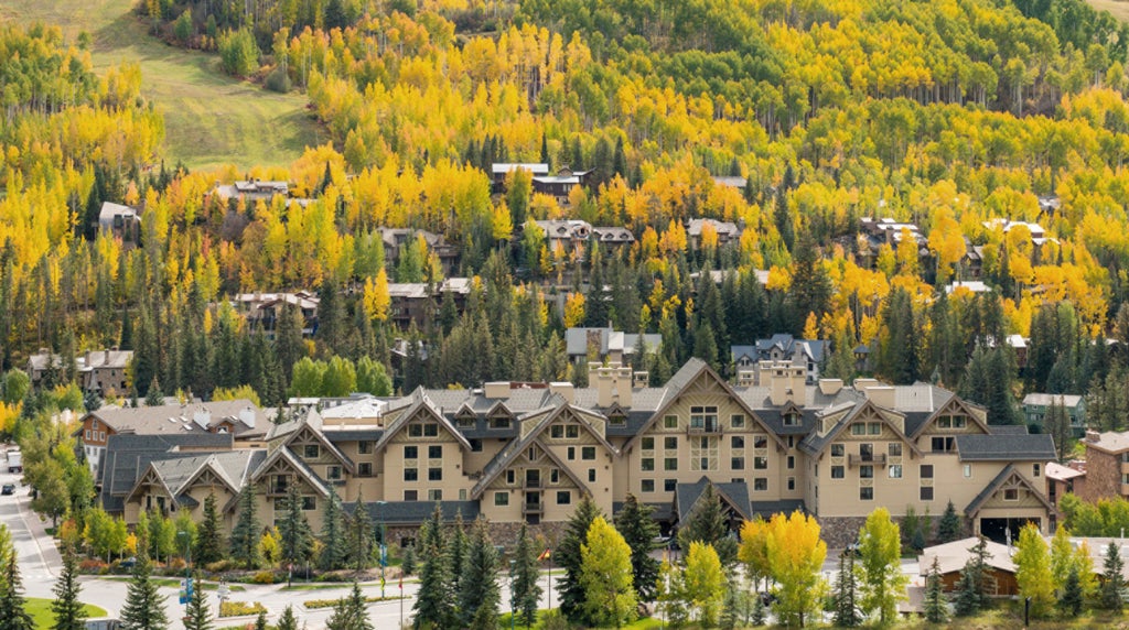 Elegant mountain lodge with stone facade, arched windows and snow-covered peaks behind, featuring upscale Four Seasons branding at dusk