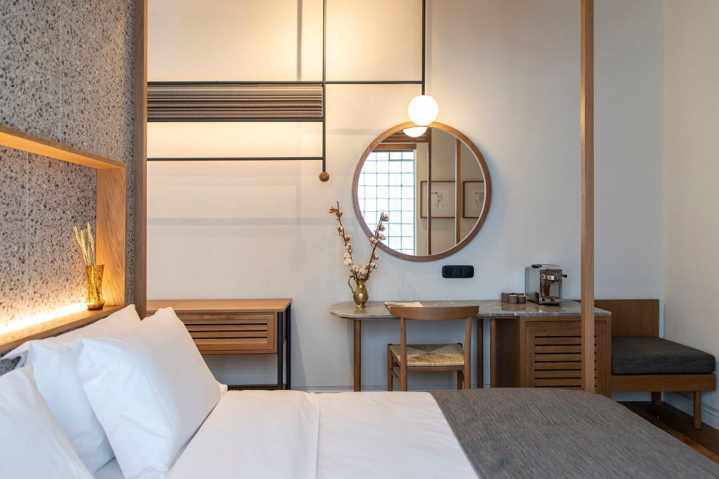 Spacious modern hotel room with minimalist design, wooden floors, white walls, large bed, and expansive windows overlooking Athens cityscape at golden hour