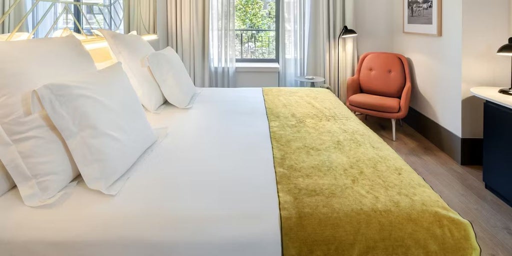 Luxurious deluxe hotel room with modern design, floor-to-ceiling windows overlooking Madrid's cityscape, elegant contemporary furnishings, and sophisticated neutral color palette