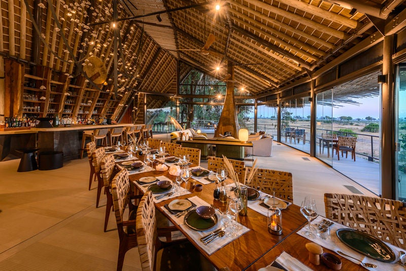 Elevated luxury safari lodge with thatched-roof suites nestled among palm trees overlooking the Okavango Delta's floodplains at sunset