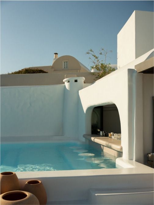 Luxurious white-washed Cycladic hotel with infinity pool overlooking azure Aegean Sea, featuring minimalist architecture and stunning sunset view in Oia, Santorini