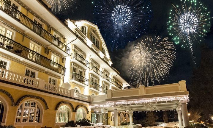 Luxurious Swiss alpine hotel with grand white facade, ornate balconies, and snow-capped mountain backdrop in scenic destination of scenset