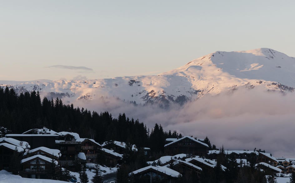 Elegant alpine hotel with sloped wooden roof nestled in snowy French Alps, featuring stone facade and panoramic mountain views