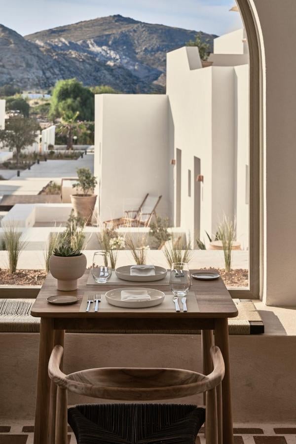 Minimalist white-walled Greek hotel exterior with stone archways, sunlit terraces and elegant pool surrounded by native Mediterranean plants