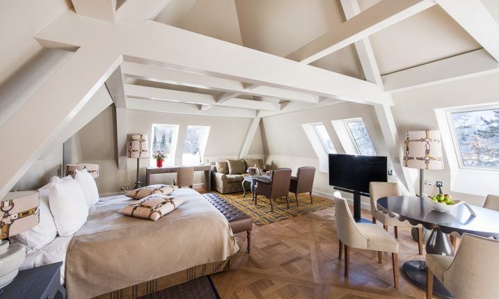 Opulent Swiss alpine suite with panoramic mountain views, elegant cream and gold decor, plush king bed, and crystal chandelier in luxurious hotel bedroom