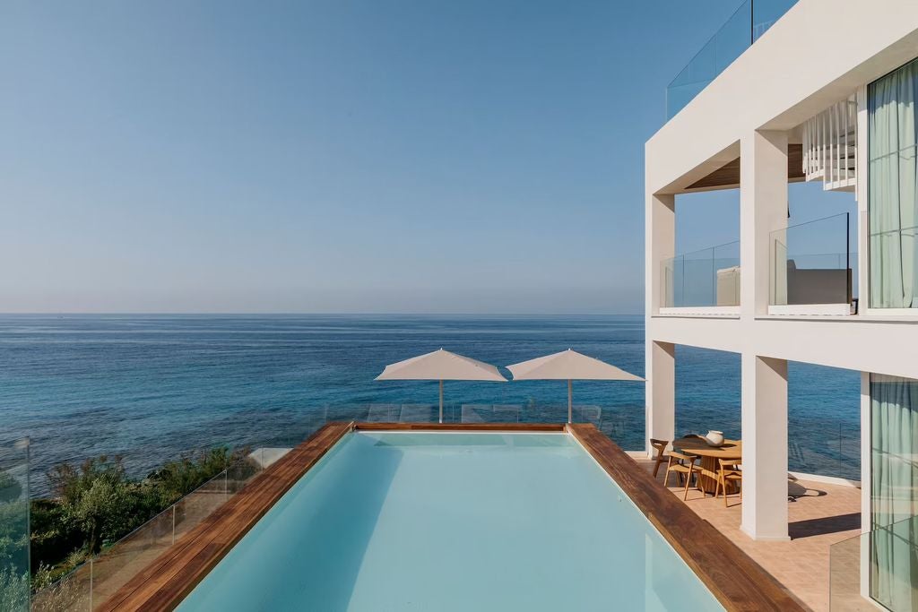 Sleek white Mediterranean hotel overlooking turquoise sea, featuring modern balconies, palm trees and a pristine infinity pool