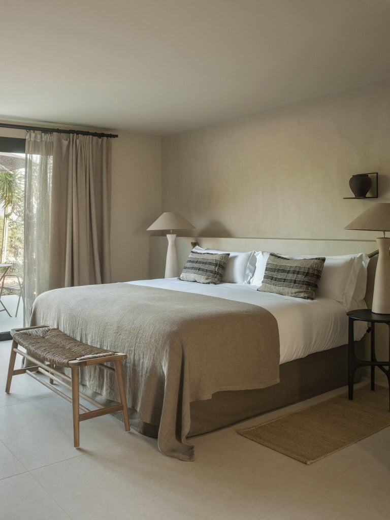 Spacious deluxe suite with elegant white interiors, large windows overlooking Mediterranean landscape, modern minimalist design with luxurious king bed and wooden accents