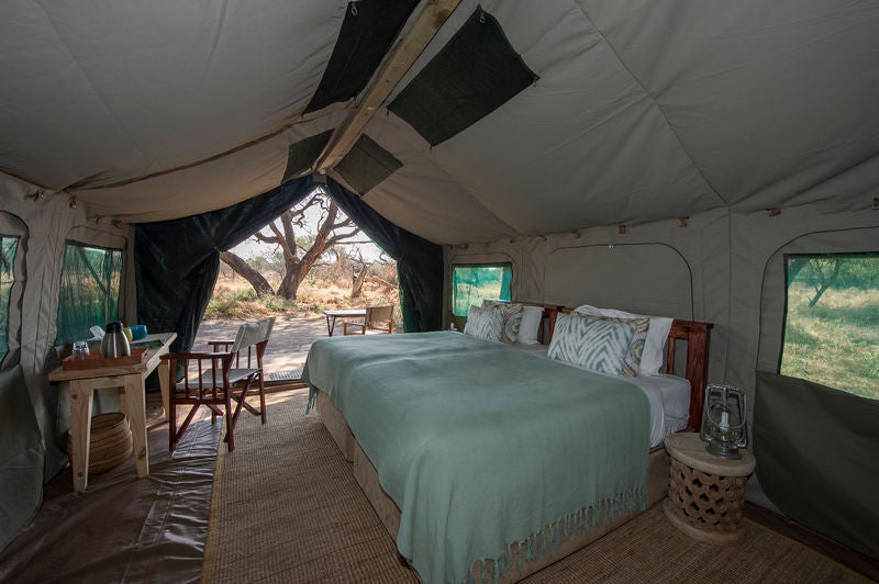 Elevated wooden safari lodge with canvas walls overlooking lush wetlands, featuring a private deck and infinity plunge pool at sunset