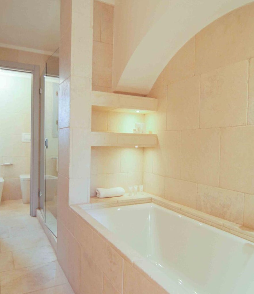 Elegant Italian hotel suite with vaulted stone ceiling, arched alcove bed, rustic chandelier and white linens against cream walls